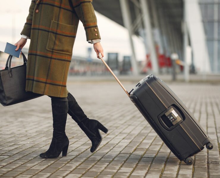 stylish woman with suitcase and bag walking on street near modern airport terminal